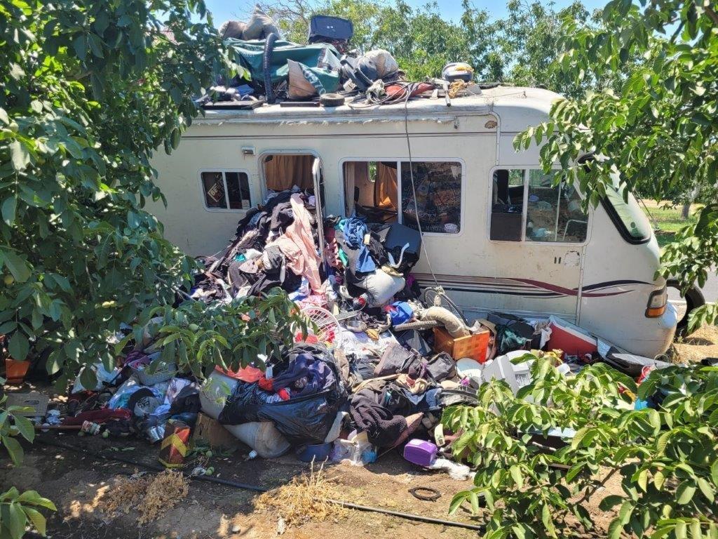 RV dumped in an orchard with debris surrounding it.